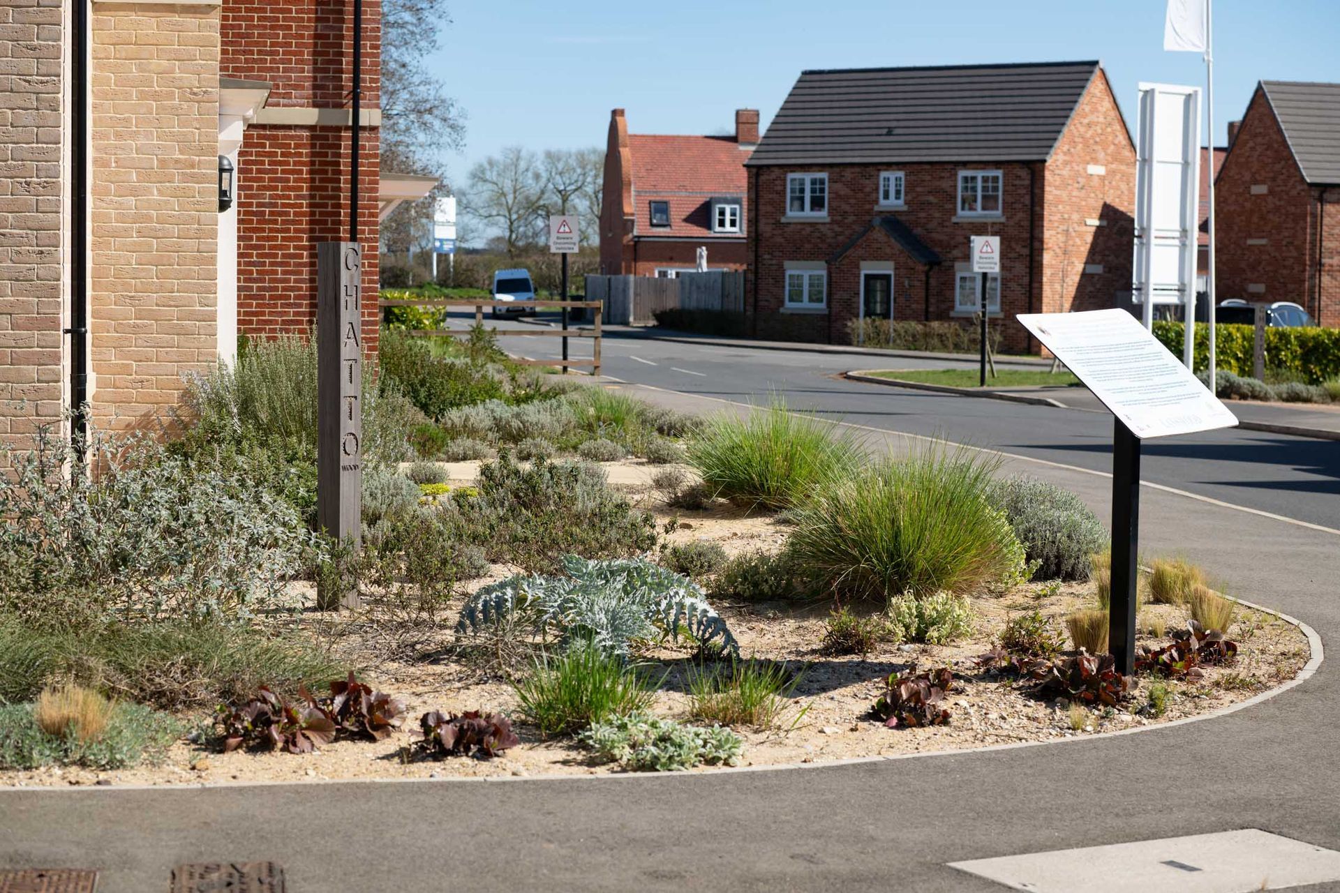 Landscaped roundabout with signage; new housing development in background.