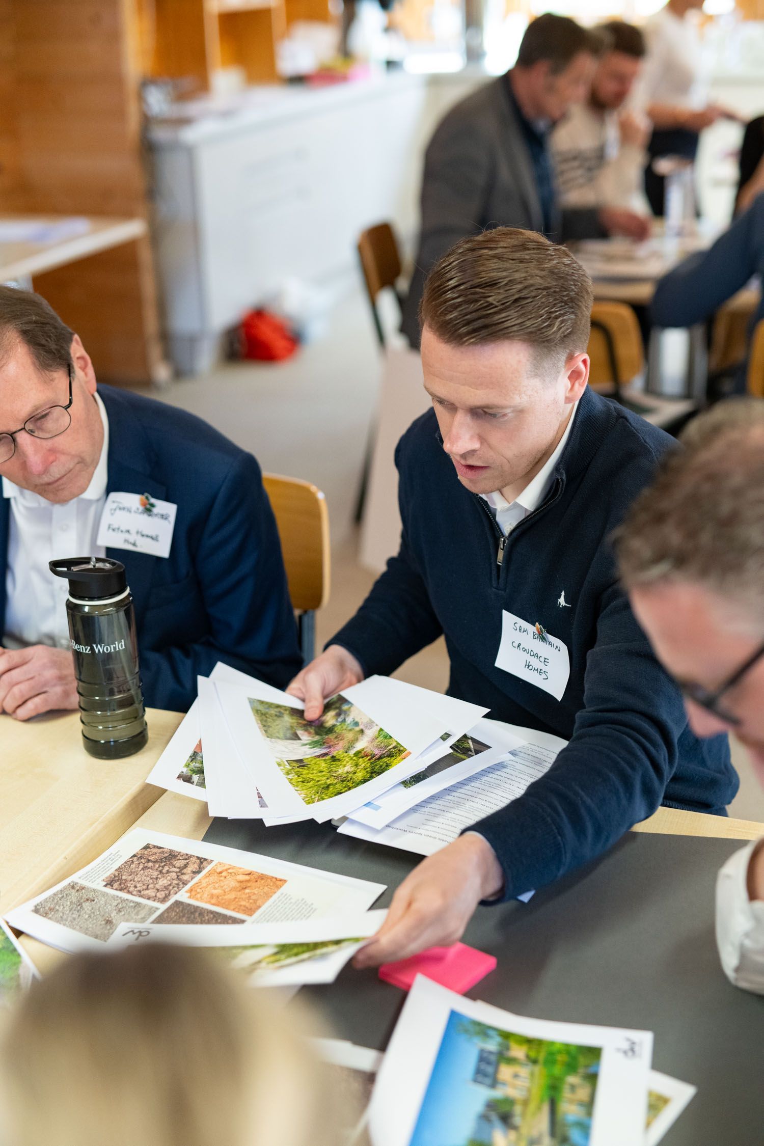 Men at a table reviewing printed materials during a meeting. Light colors, indoor setting.