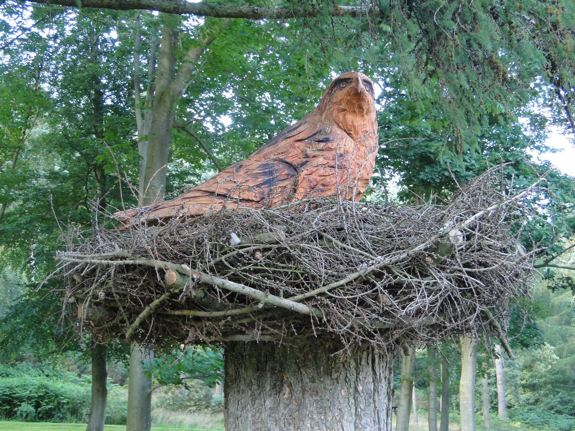 Brown and orange owl statue in a large nest atop a tree stump in a forest.
