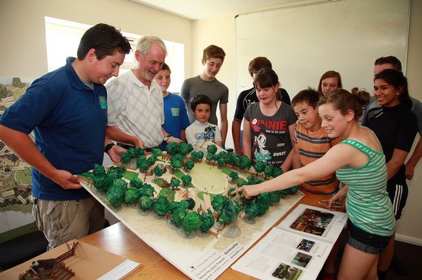 Group of people examining a model of a park. They are gathered around a table indoors, looking at the model.