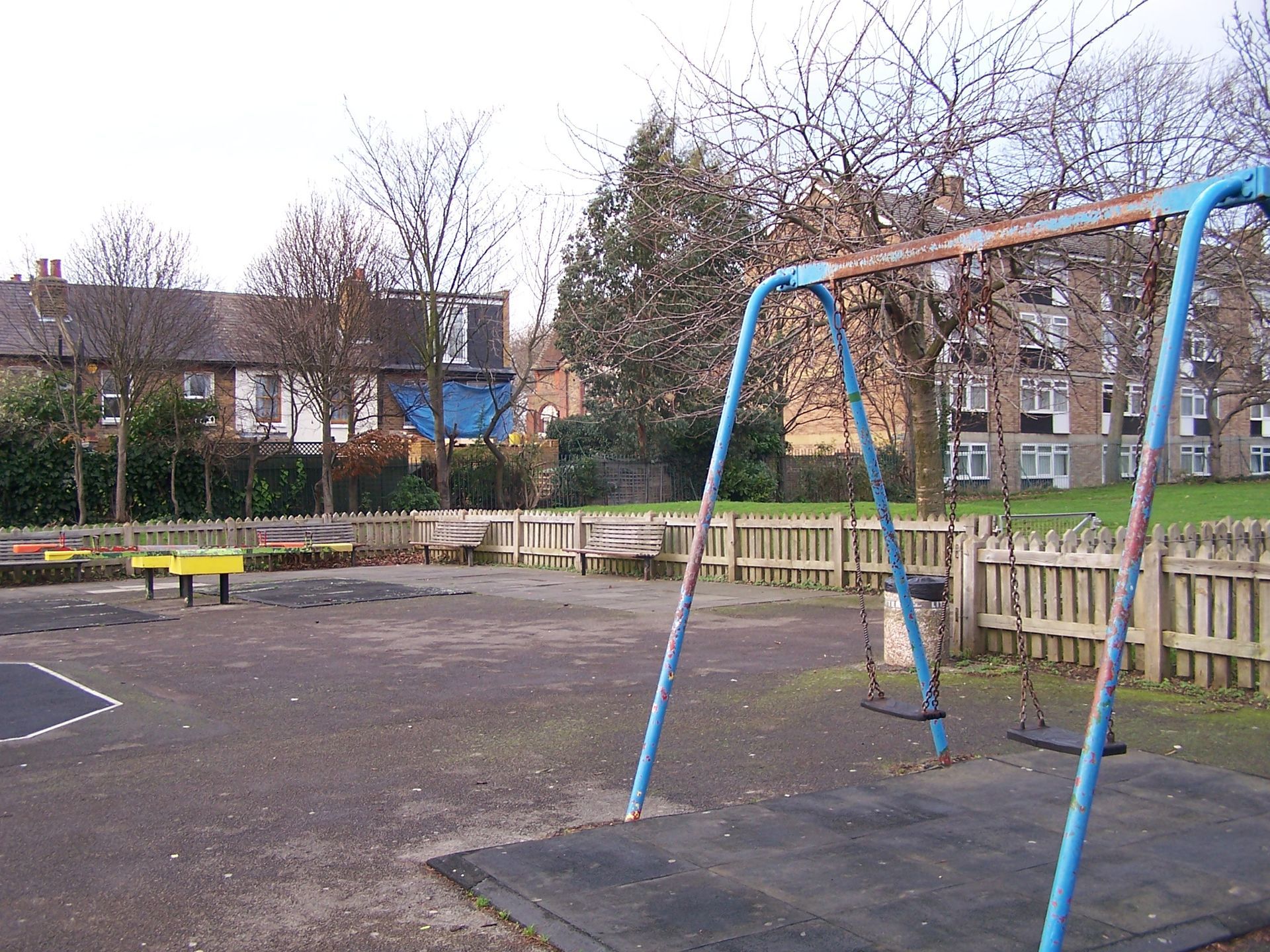 Playground with swings, a wooden fence, and houses in the background.