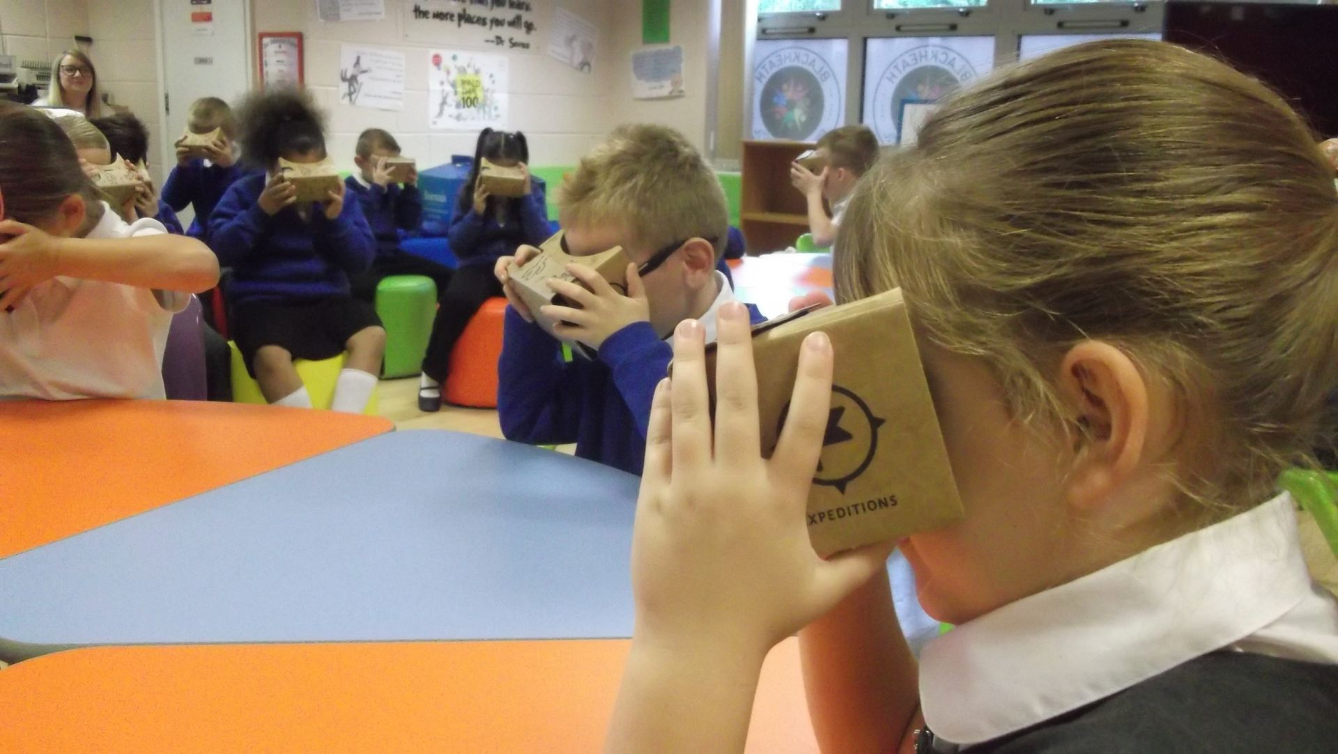 Children in a classroom wearing cardboard VR headsets, looking at a virtual reality.