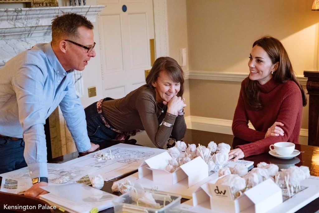 Man and two women at a table with architectural models and blueprints, smiling. Interior setting.