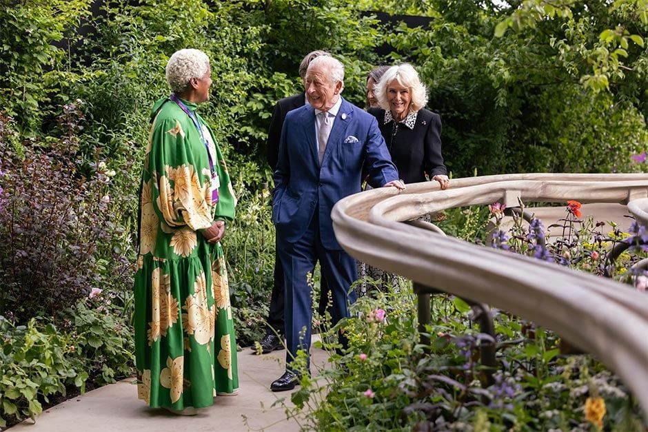 The King and Queen conversing in Arit Andersons lush Parkinsons UK garden beside a curved stone railing