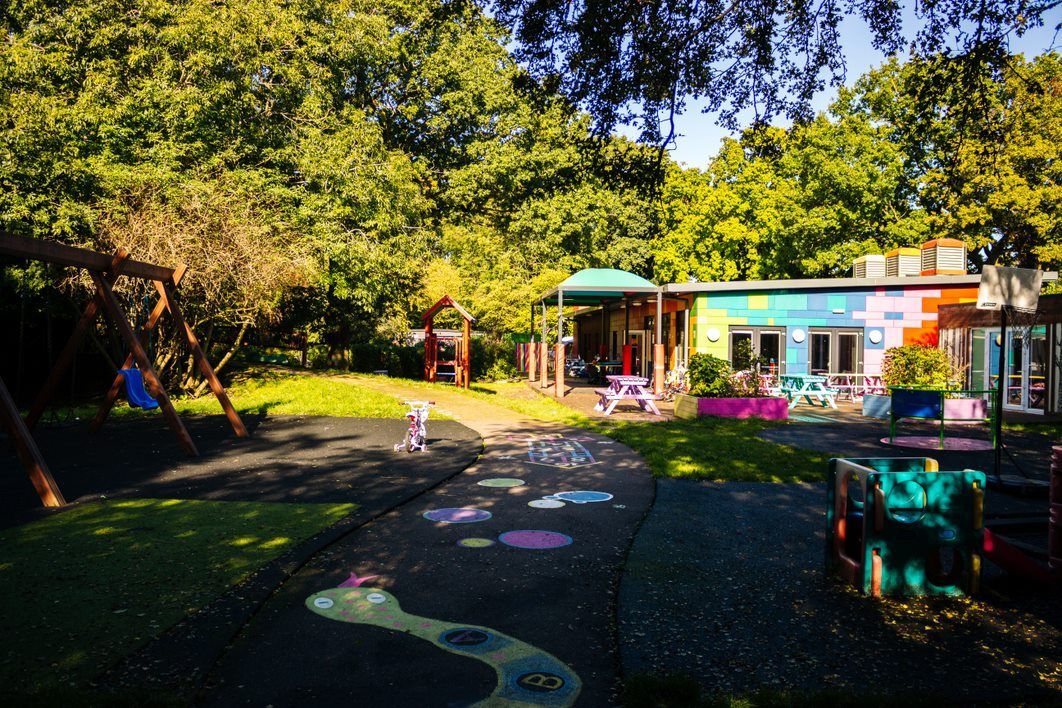 Playground with colorful building, trees, swing set, and pathway.