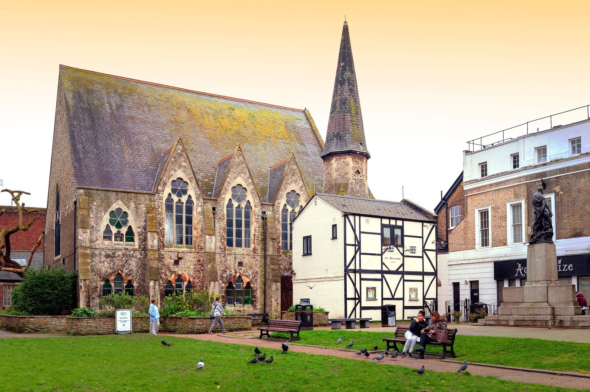 Church with spire, half-timbered building, and people on a green in a town square.