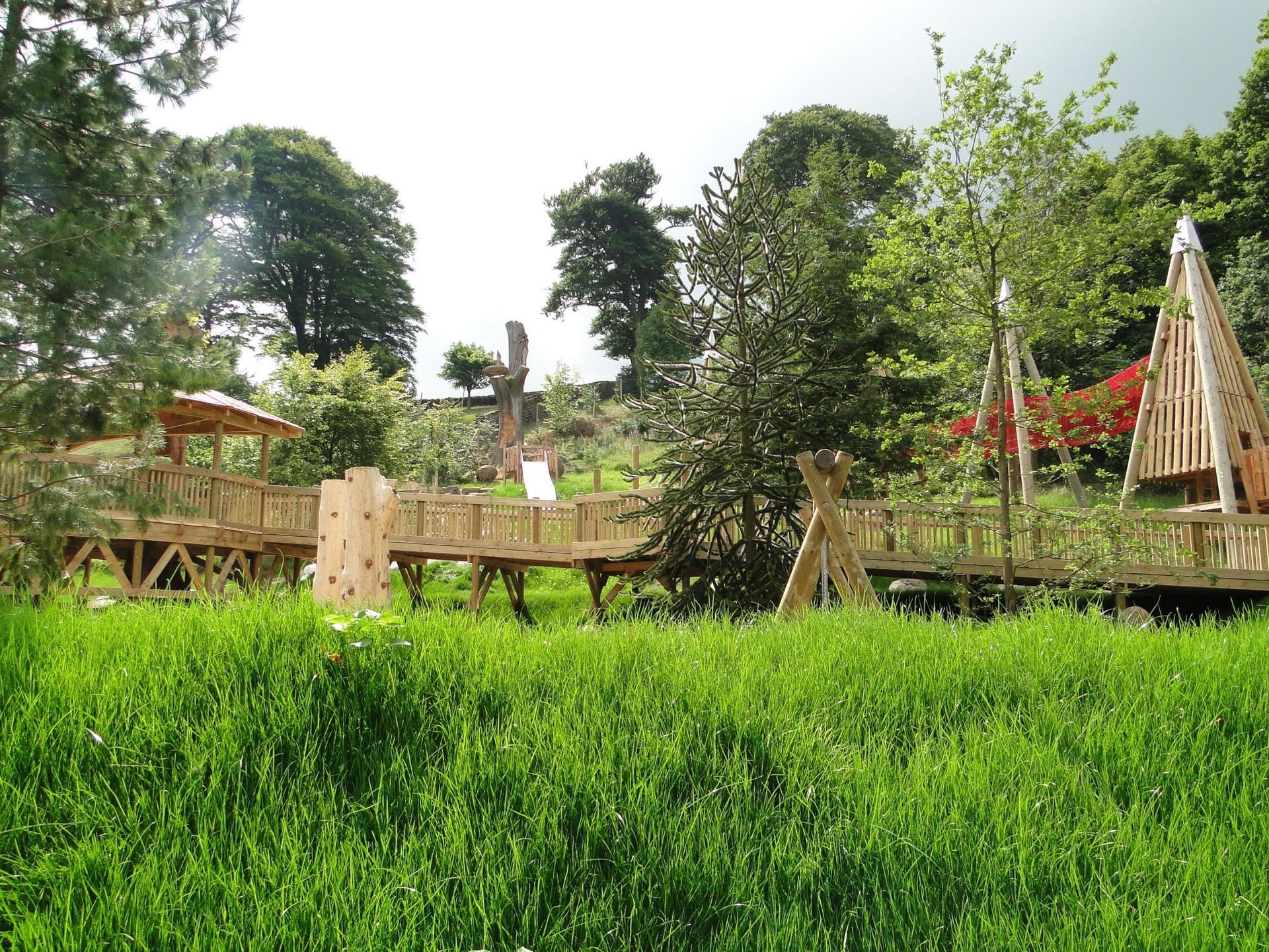 Wooden playground structure in a grassy field with trees in the background.