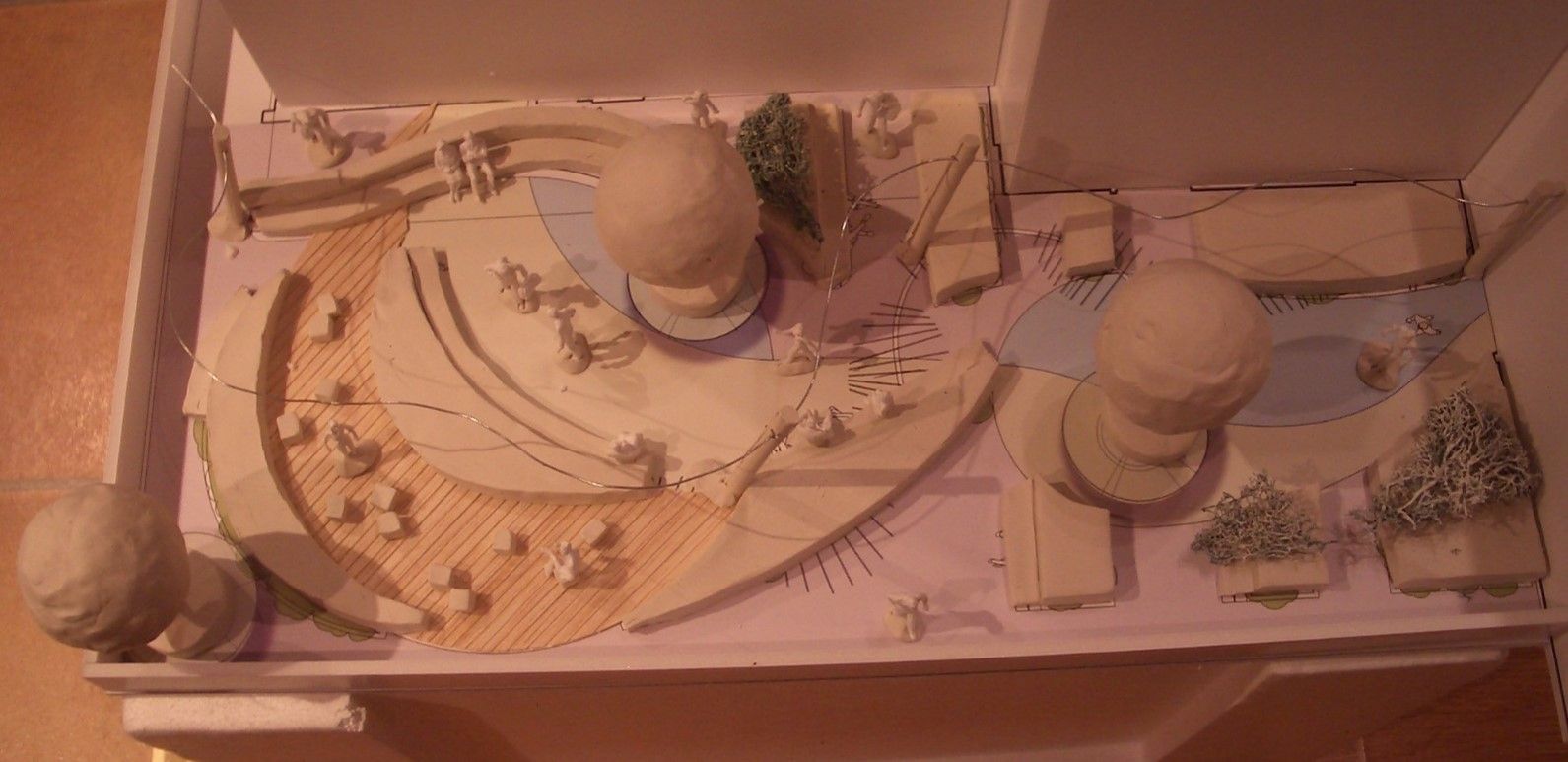A model of a landscape design, featuring rounded structures, water features, and trees, in a white box.
