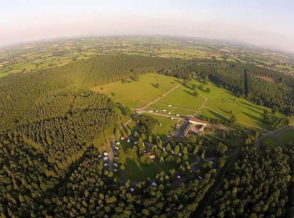 Aerial view of a campsite in a forest, with green trees, a clearing, and scattered tents.