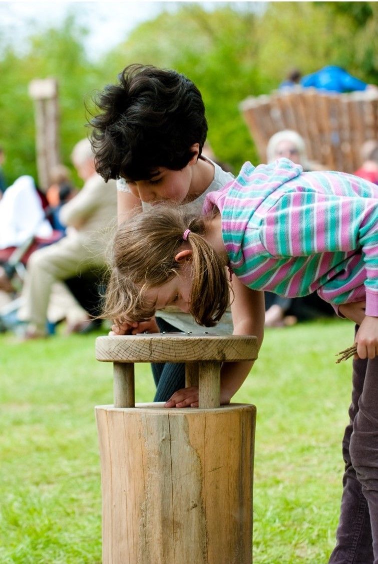 Two children leaning over a wooden structure outdoors, looking down with curiosity.