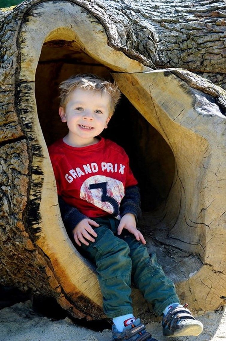 Young child smiling in a hollow log, wearing a red