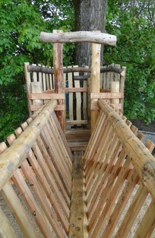 Wooden playground structure, with a bridge and tower against a tree, natural colors.