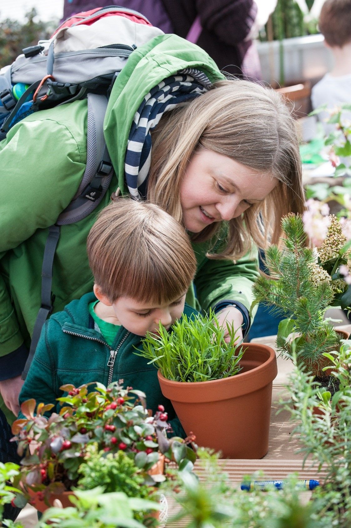 Woman and child looking at plant in pot at outdoor market; child smelling it.