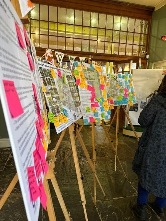 Event showcasing posters on easels, covered in sticky notes, person viewing them.