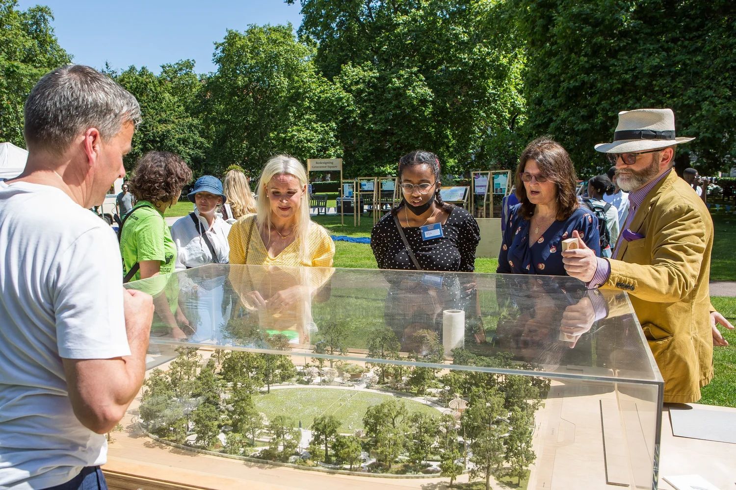 People looking at a landscape model outdoors, trees and sky in background.