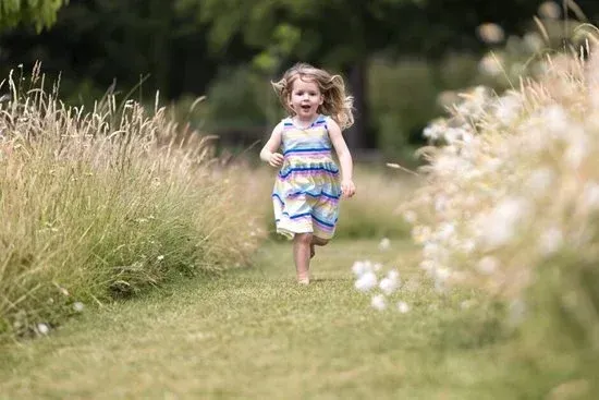 A person in a colorful dress runs along a grassy path between tall stalks of wild grass and white flowers.