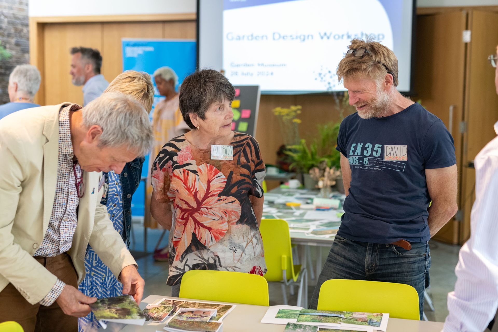 People at a garden design workshop, examining photos on a table. Smiling, in a bright room.