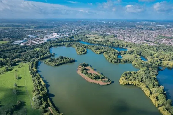 Aerial view of lakes surrounded by green trees, with a town in the background under a blue sky.