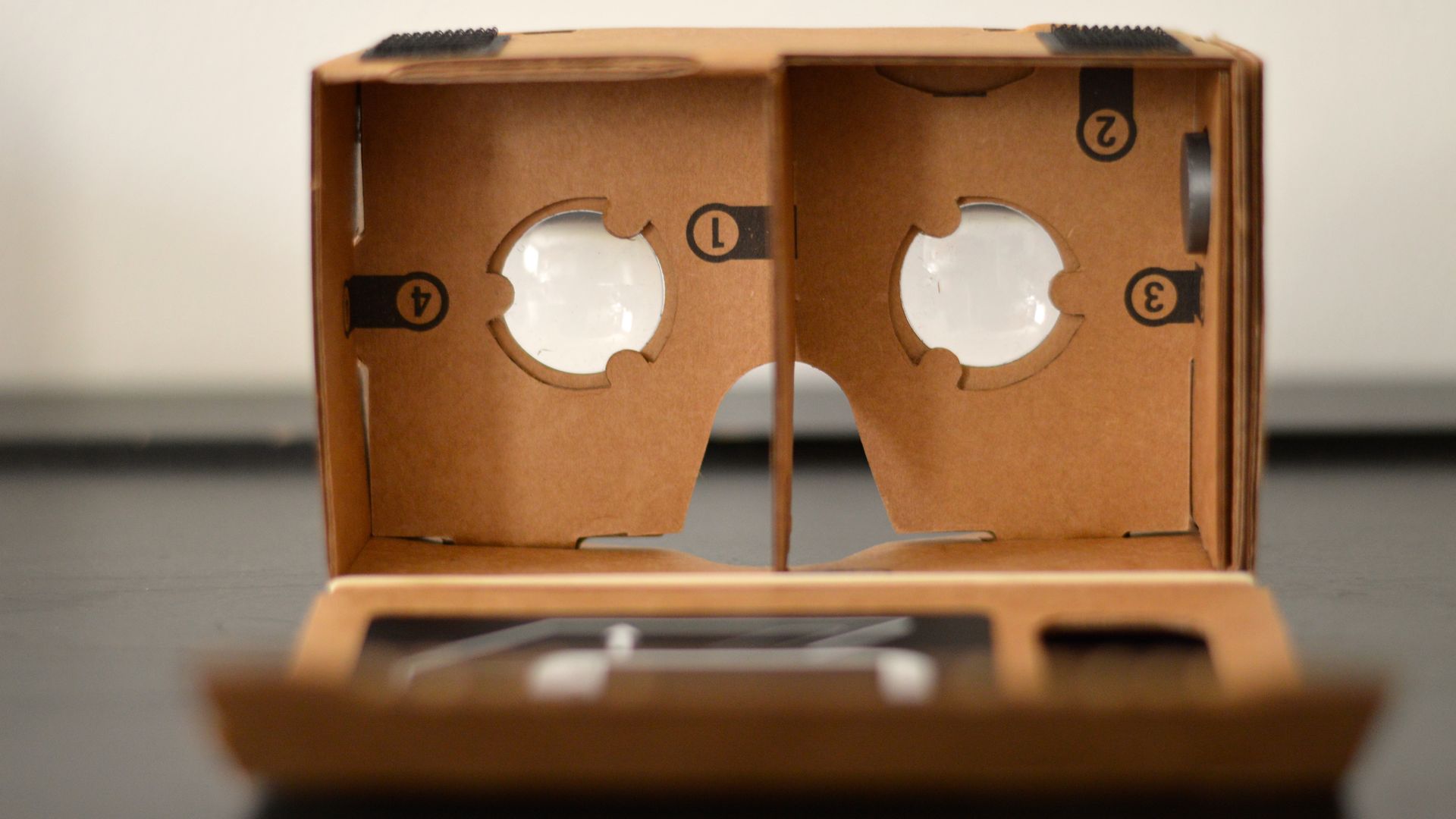 Cardboard VR headset with lenses, brown, on a dark surface.