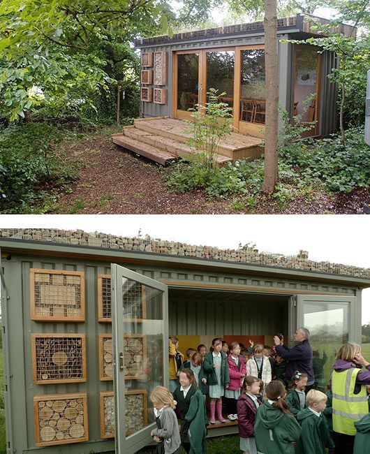 A repurposed shipping container classroom in a wooded area with a green roof, outdoor deck, and insect habitat boxes.