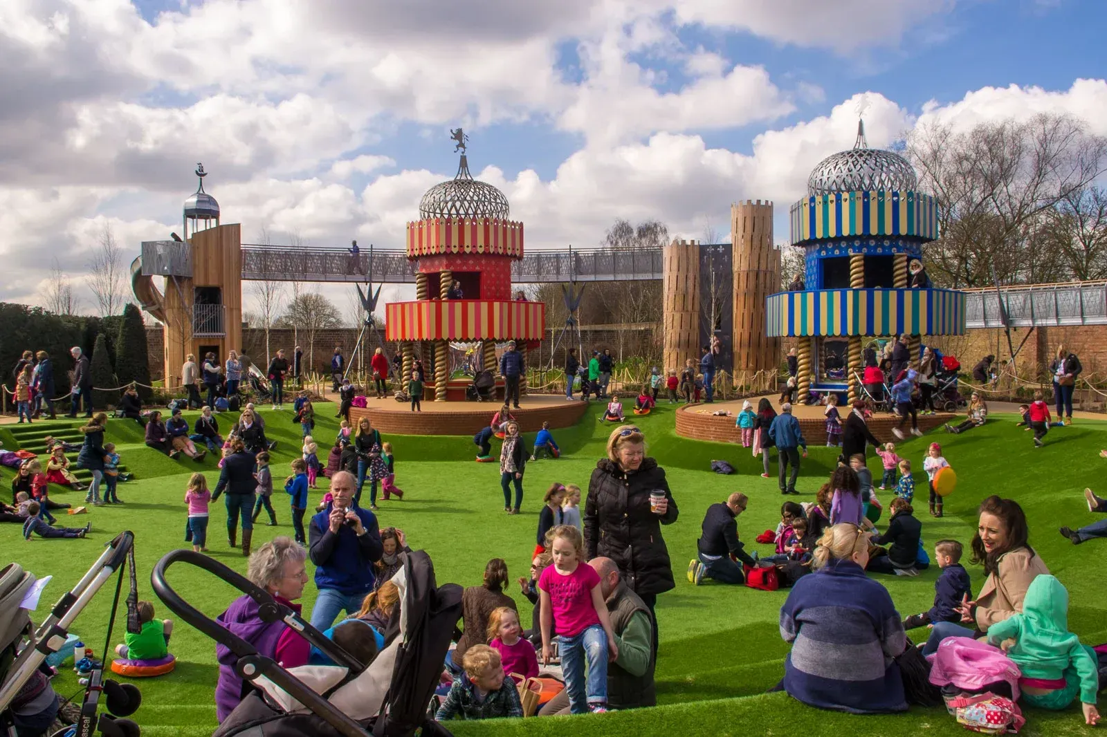 A busy outdoor playground with colorful structures and many children and adults enjoying the sunny day.