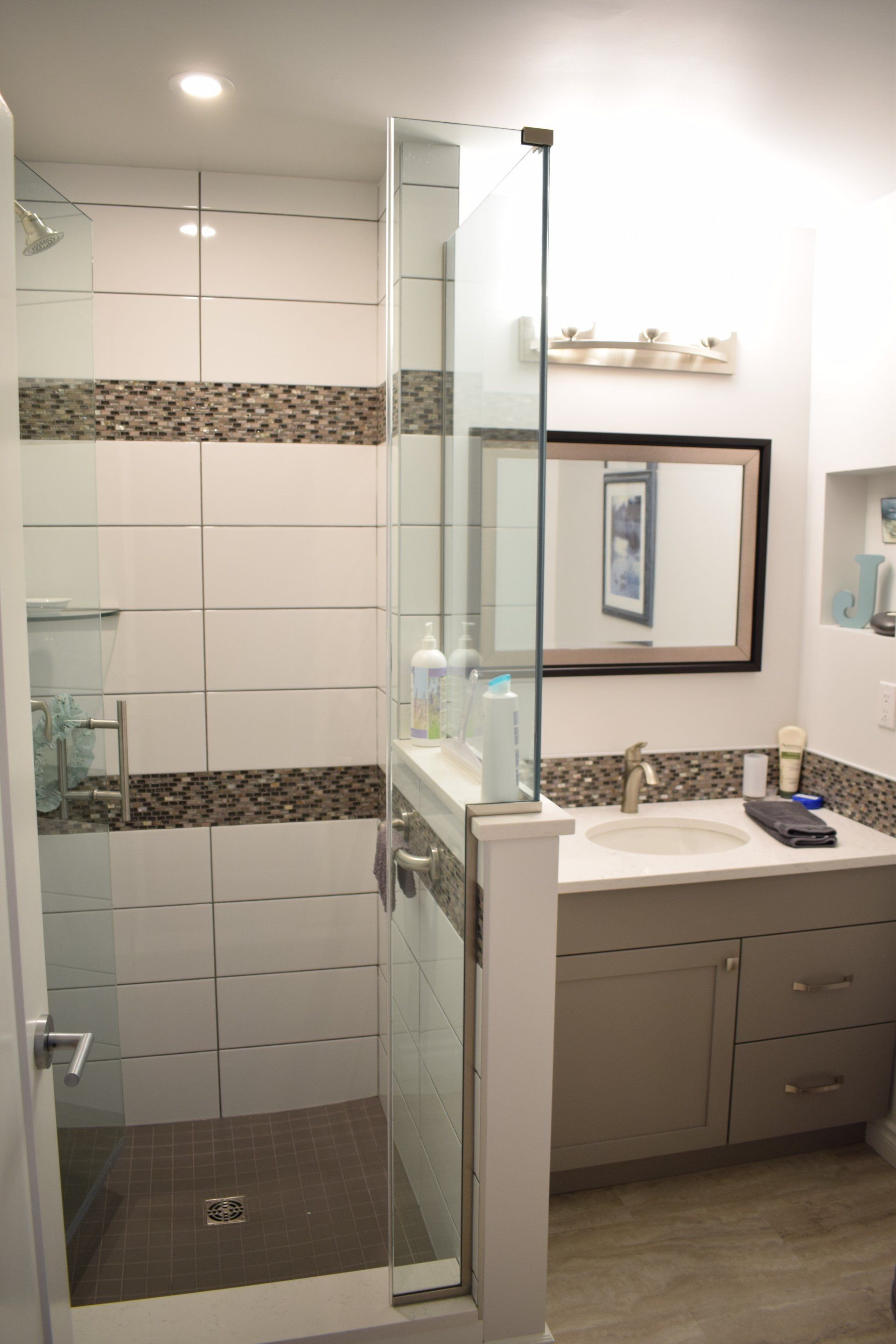A bathroom with a walk in shower , sink and mirror.