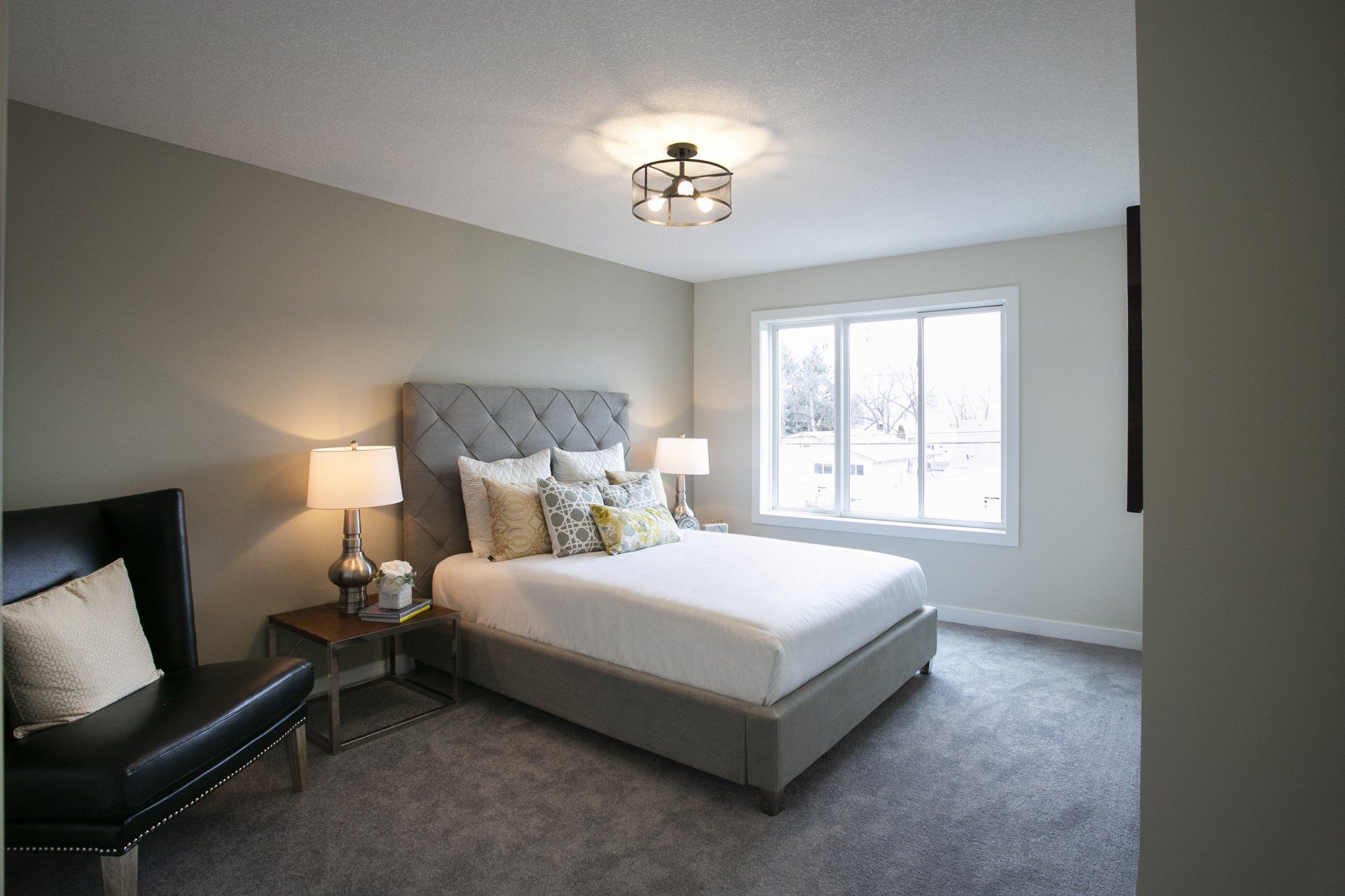 A bedroom with a bed , chair , lamps and a window.
