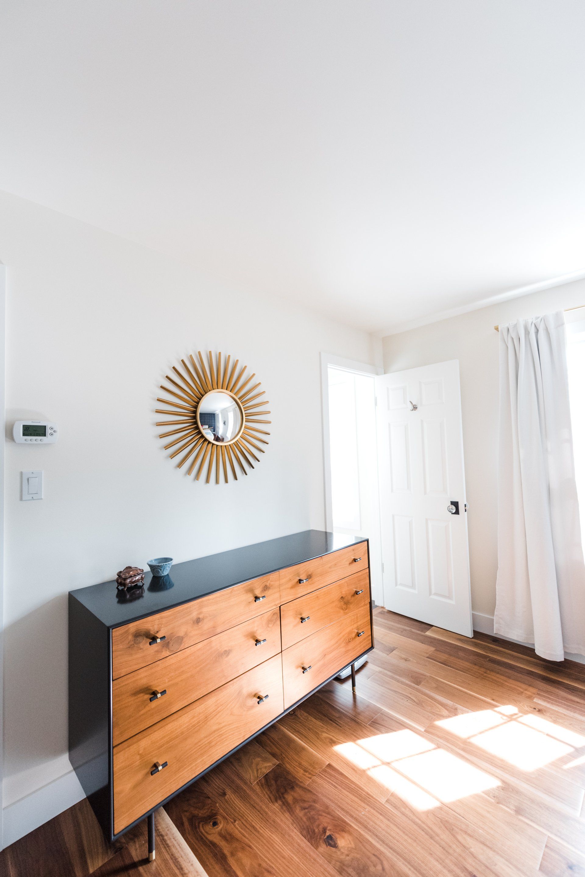 A bedroom with a wooden dresser and a mirror on the wall.