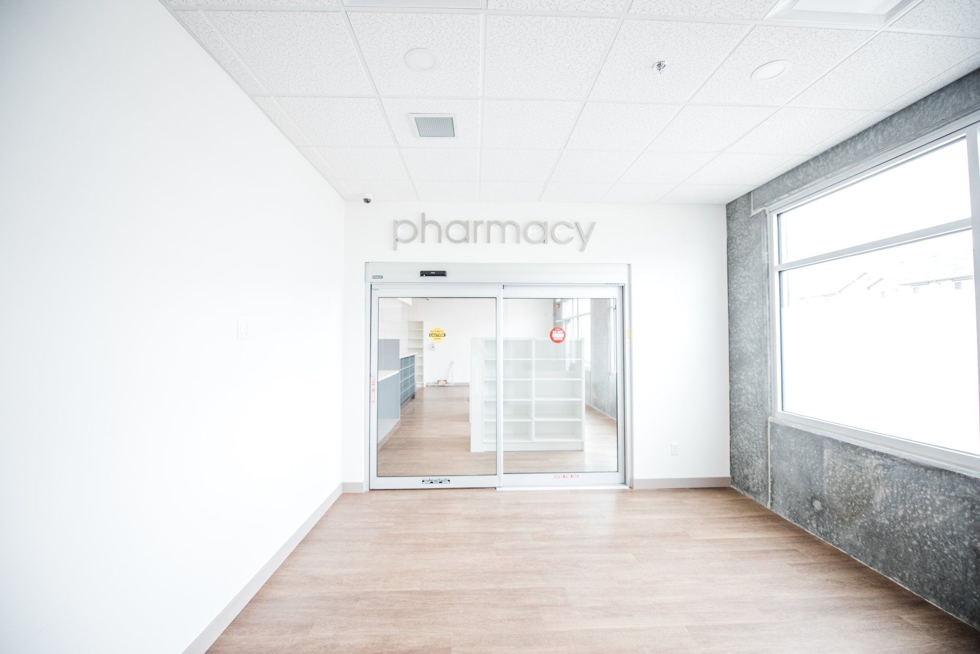 An empty hallway leading to a pharmacy with a sliding glass door.