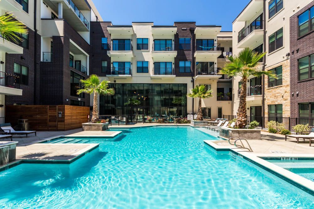 Resort-style swimming pool in a modern apartment complex courtyard with palm trees, lounge chairs, and multi-story residential buildings in the background at Marq 31 in Houston, TX.