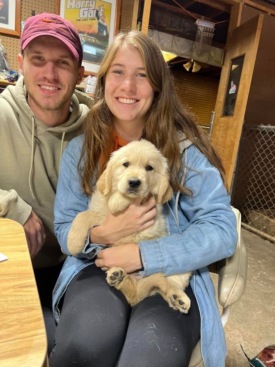 A man and a woman are holding a puppy in their arms.