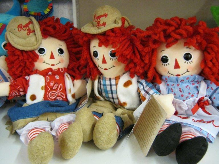 Three rag dolls with red yarn hair and cowboy hats sitting side by side on a shelf
