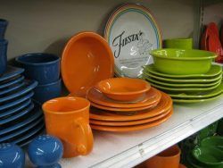 Colorful stacked plates and bowls on store shelves: blue, orange, and green dishware.
