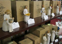 Row of handmade doll figurines displayed on shelves above stacked cardboard boxes