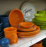 Colorful stacked dishes and mugs on a store shelf, including orange, green, blue, and white plates.