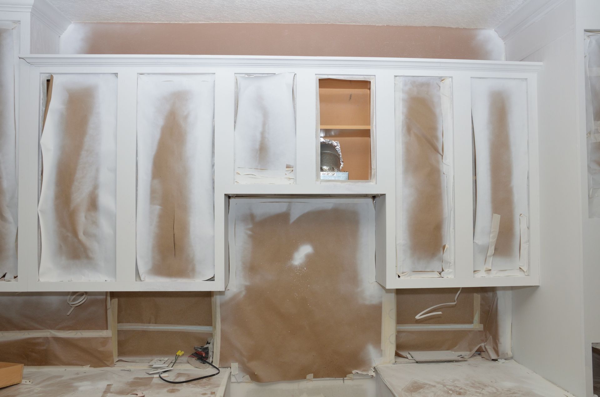 Unfinished kitchen cabinet painting project in progress, cabinets temporarily covered with protective paper