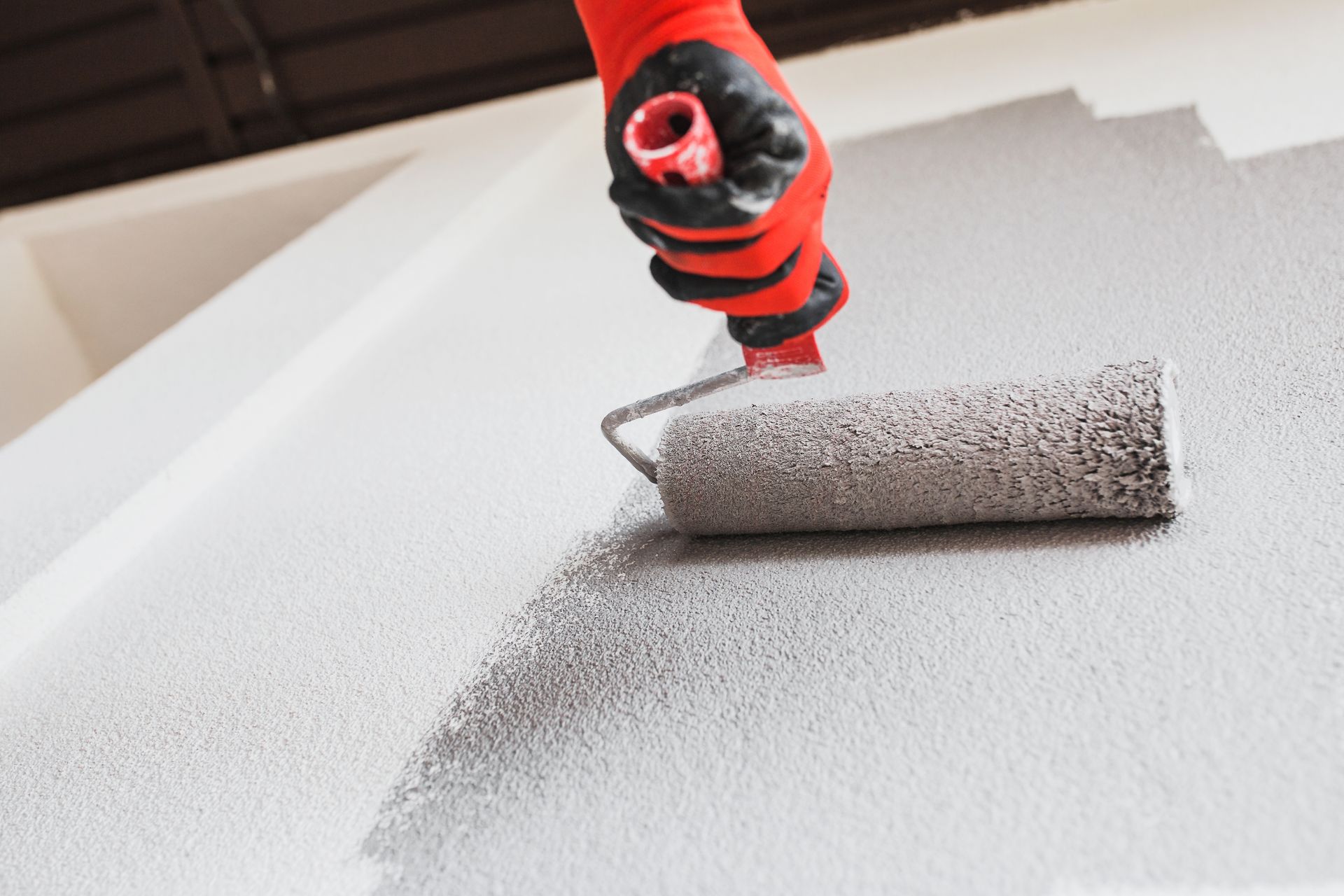 An individual using a paint roller to apply dark gray paint on a building facade during a commercial painting project, as part of a renovation.