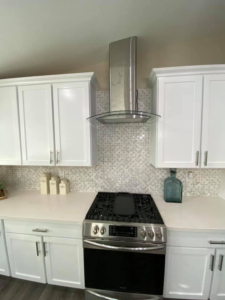 A kitchen with white cabinets , a stove , and a hood.