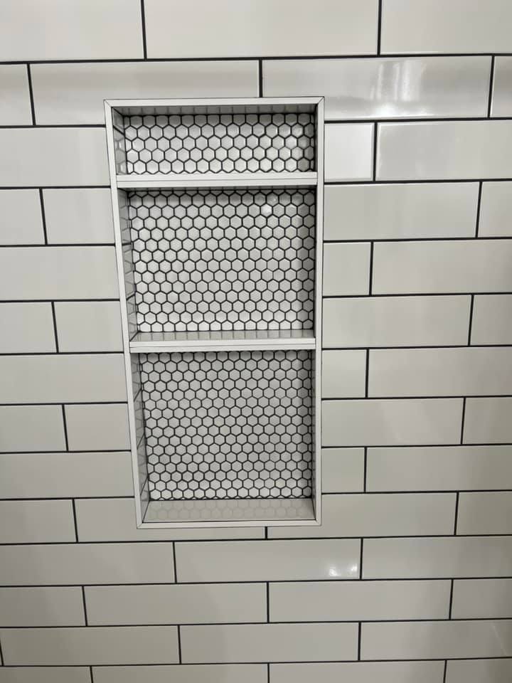 A shower niche in a bathroom with white tiles and a shelf.