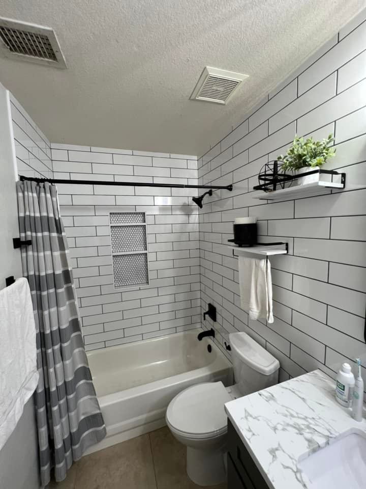A bathroom with white brick walls , a toilet , a bathtub , and a sink.