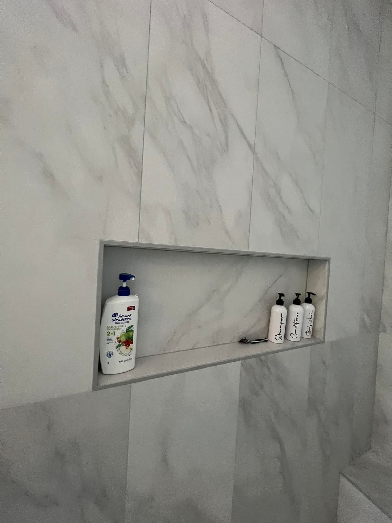 A bathroom with a shelf filled with bottles of shampoo and lotion.