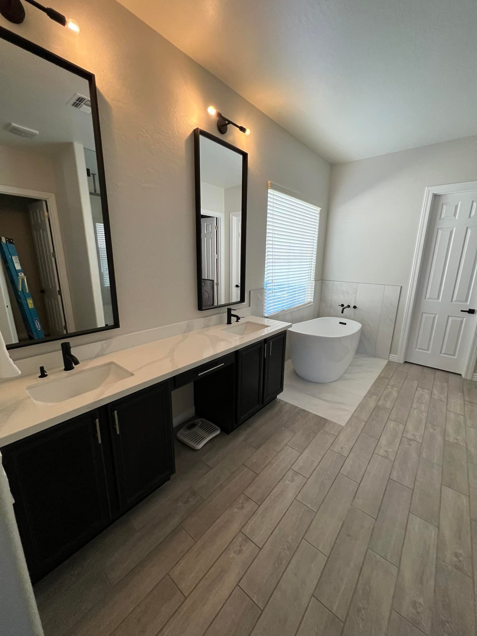 A bathroom with two sinks , two mirrors and a tub.