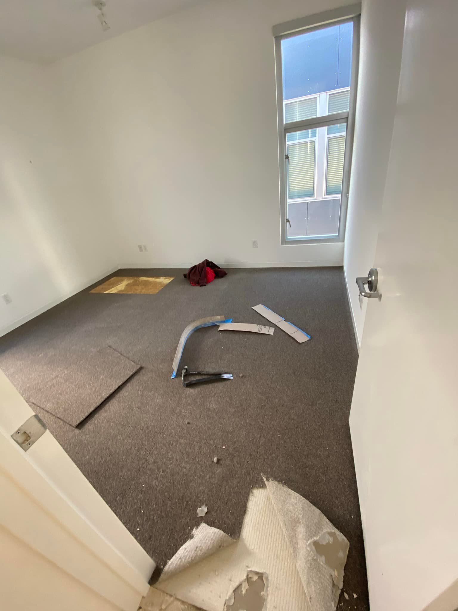 A room with a broken carpet and a window.