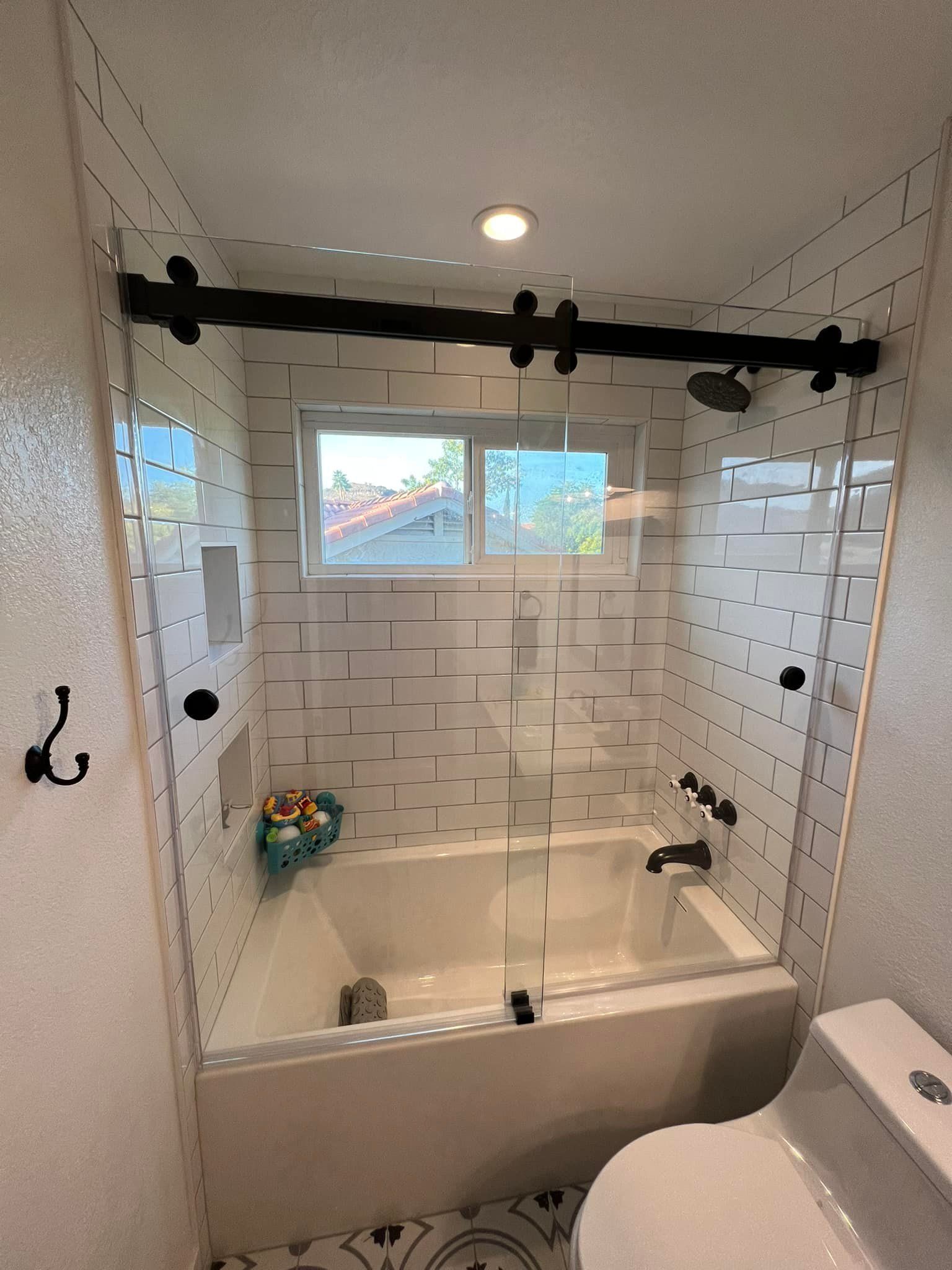 A bathroom with a tub , toilet , shower and window.