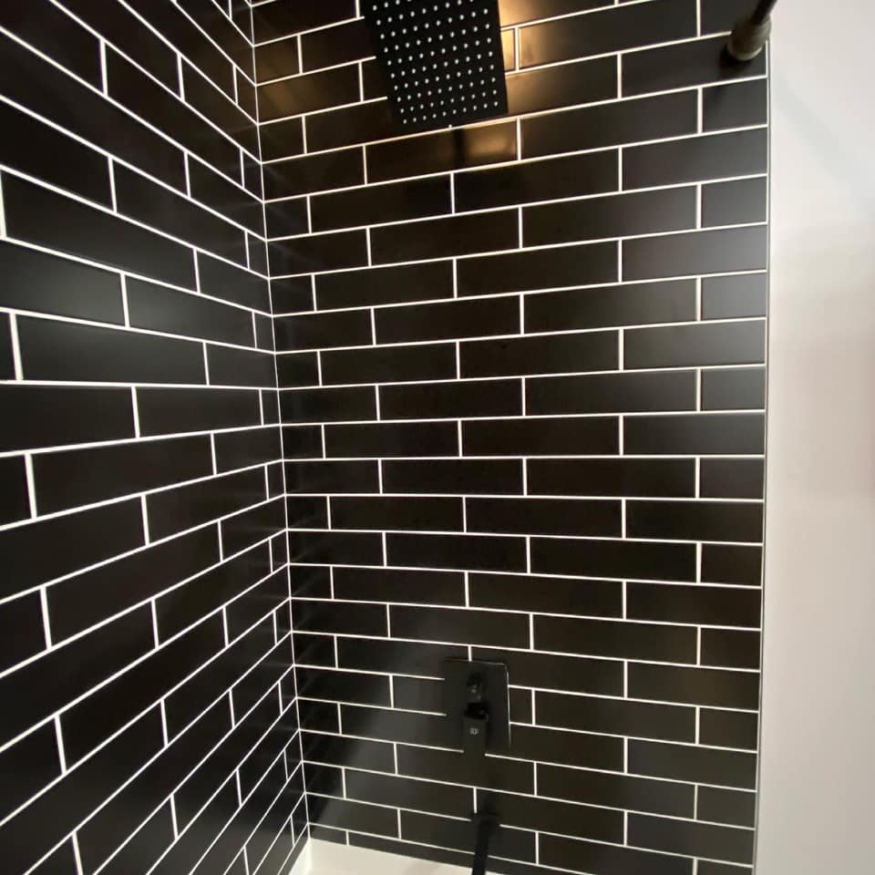 A shower with black tiles and a black shower head