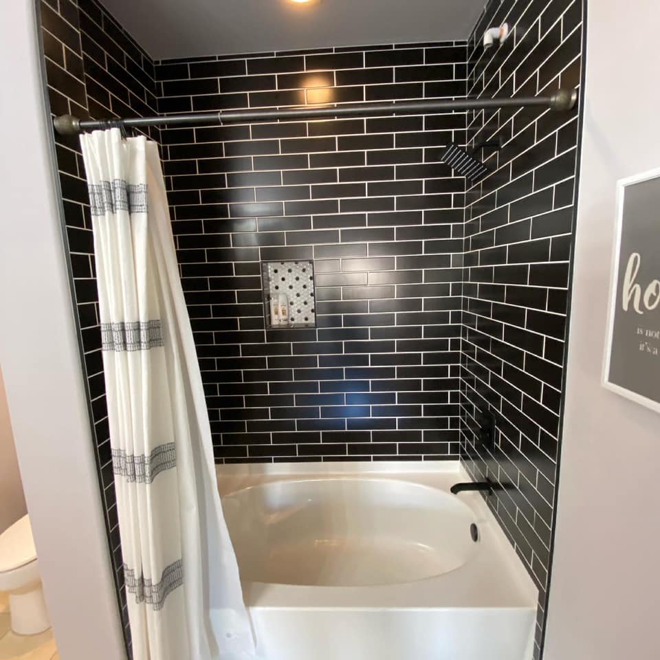 A bathtub in a bathroom with black brick walls and a shower curtain.