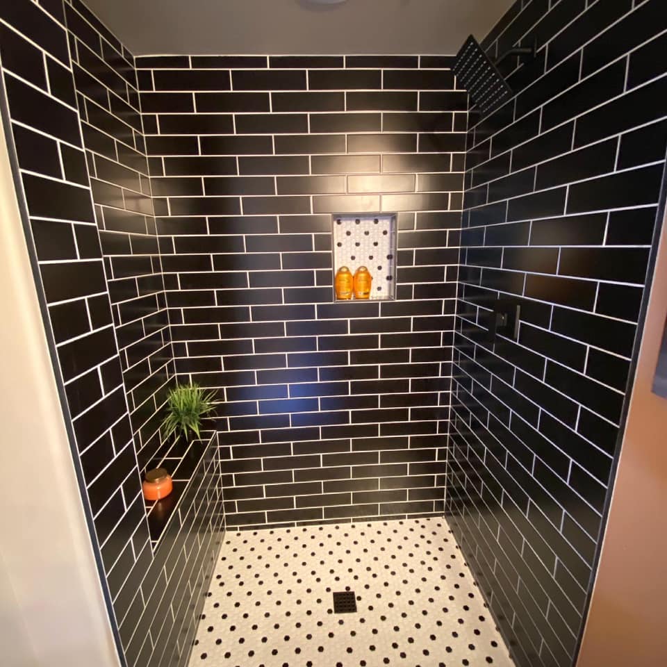 A shower with black brick walls and a white polka dot floor