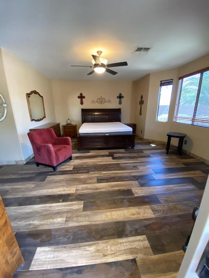 A bedroom with a bed , chair , mirror and ceiling fan.