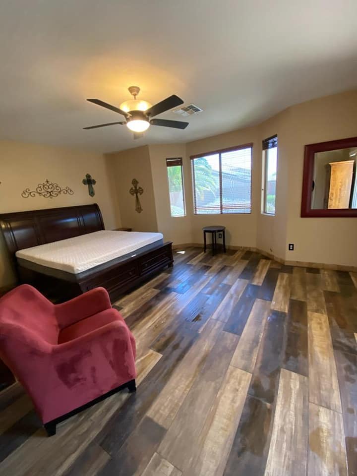 A bedroom with a bed , chair , mirror and ceiling fan.