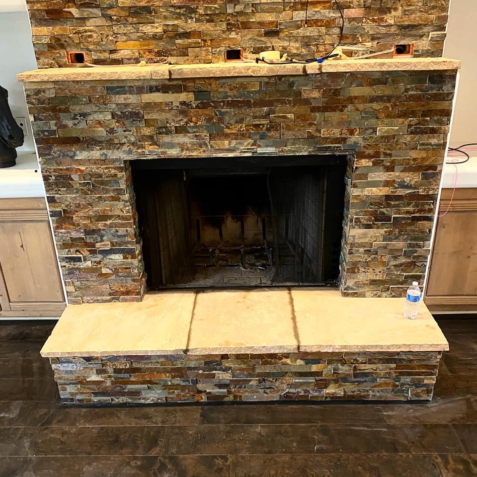 A stone fireplace in a living room with a bottle of water on the floor.